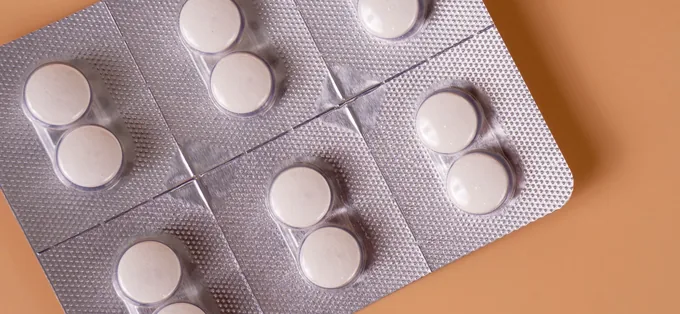 White tablets in blister packs on a peach-coloured background