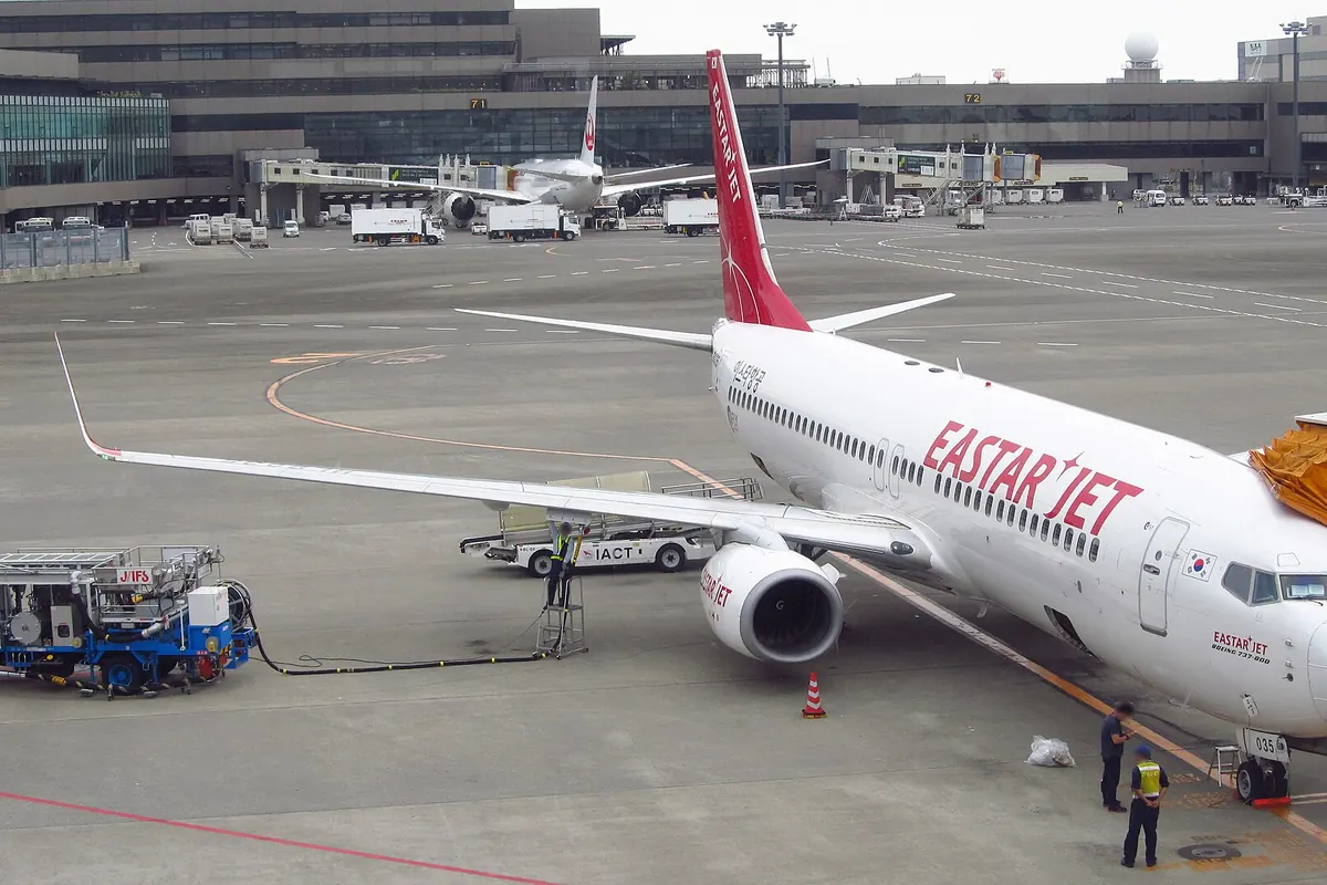 공항 계류장에 주기된 빨간 꼬리 도장의 Eastar Jet 보잉 737 기종, 근처에 급유차