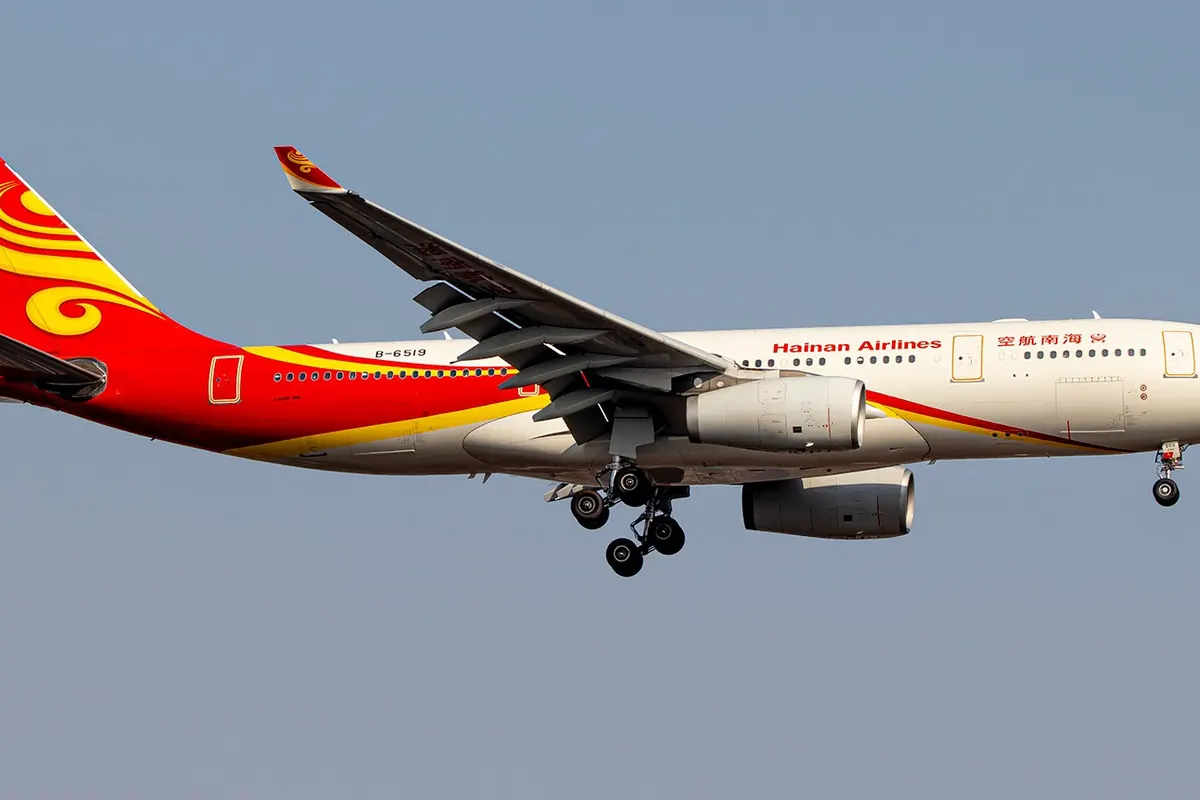 A Hainan Airlines Airbus A330 aircraft in flight with its landing gear down, showing a red tail with a golden phoenix design