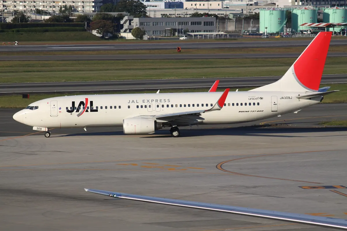 A JAL Express Boeing 737 aircraft with a red tail and crane logo parked at Osaka Itami Airport