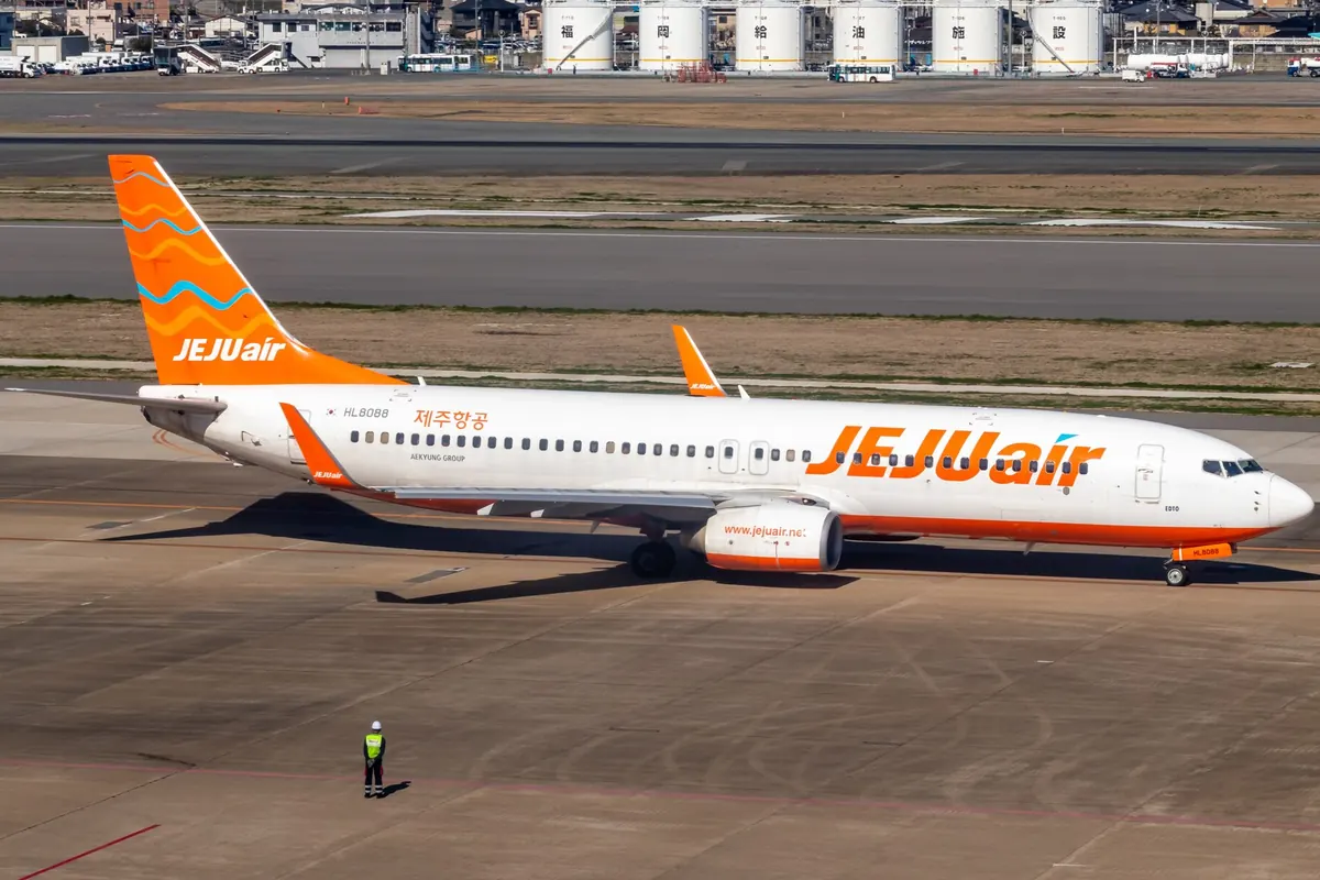 후쿠오카 공항에 주기된 Jeju Air 보잉 737 기종, 꼬리는 주황색 파도무늬이며 근처에 지상 직원