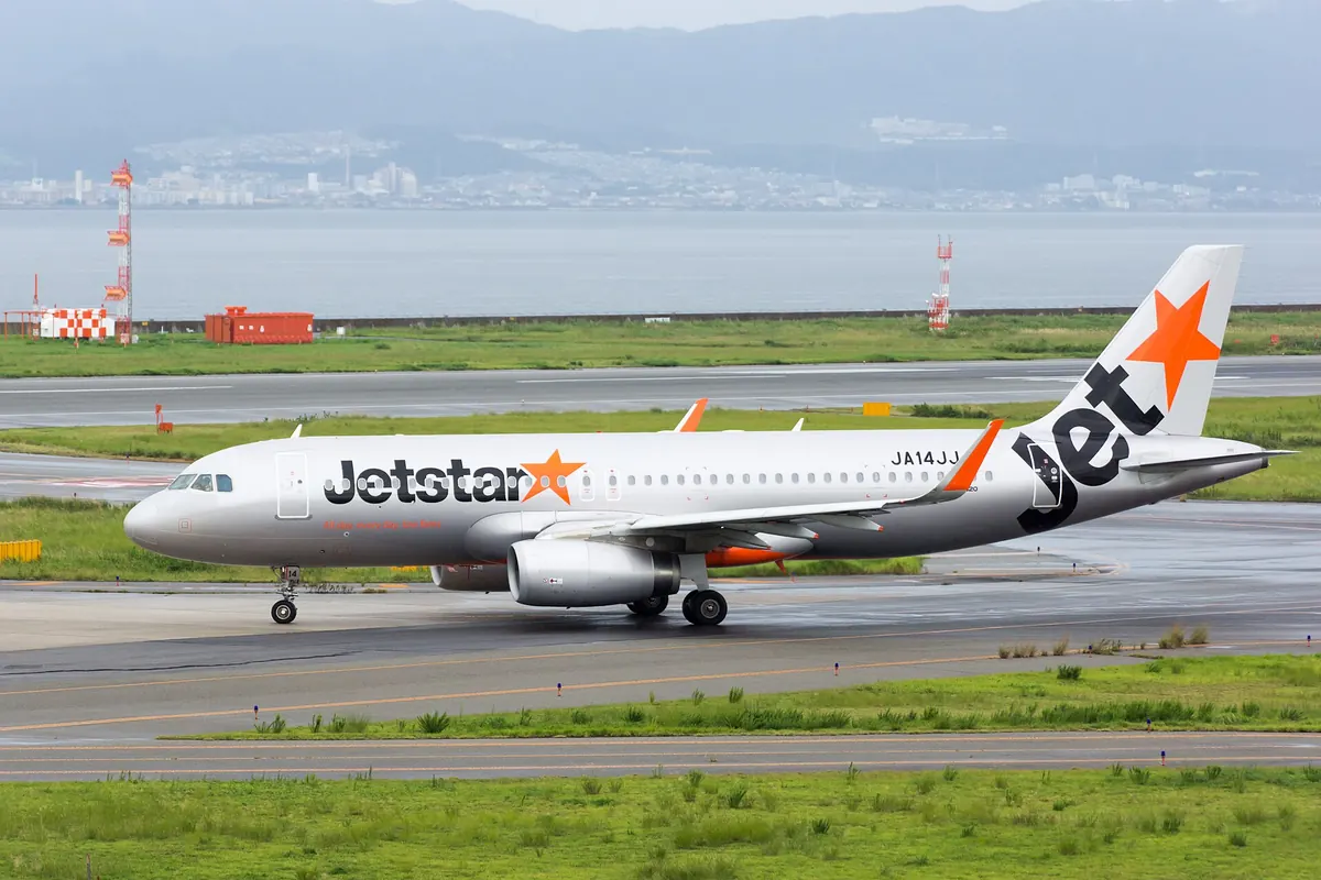 A Jetstar Japan Airbus A320 aircraft taxiing on the runway, with an orange star tail and the sea in the background