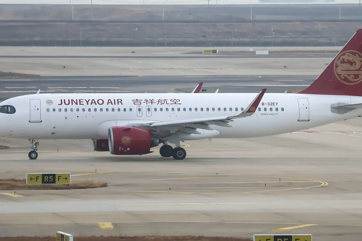 A Juneyao Air Airbus A320neo with a gold emblem on its red tail, on a taxiway at Shanghai Pudong Airport