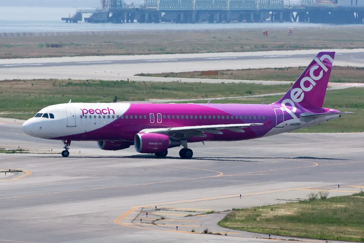 A pink and white Peach Aviation Airbus A320 taxiing at an airport