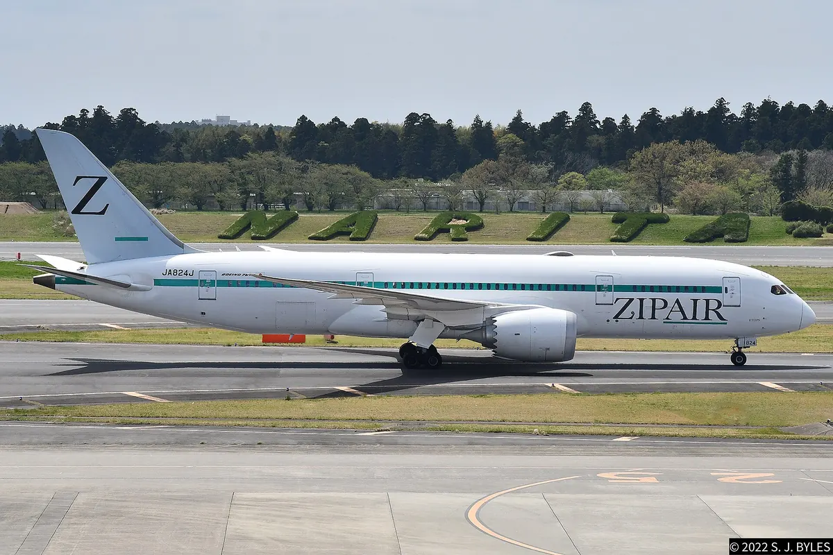 A ZIPAIR Boeing 787 taxiing at Narita Airport, showing a white fuselage, green stripe and black Z tail logo