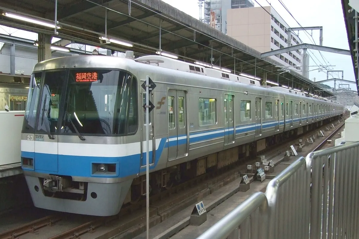 駅のホームに停まる、青い帯が入った銀色の福岡市地下鉄車両と、赤い「福岡空港」の行先表示