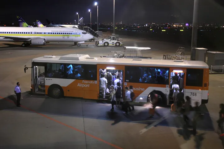 An orange and white Airport Limousine bus with passengers boarding at night at Haneda Airport