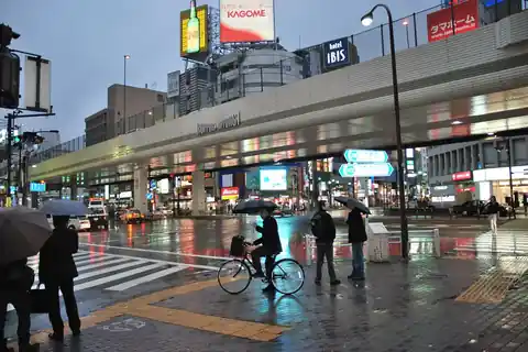 Roppongi Crossing in Tokyo, with lit building signs above the street and people holding umbrellas