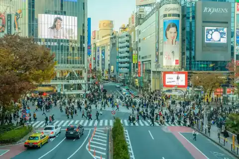 Shibuya Scramble Crossing in Tokyo, with crowds of pedestrians crossing in all directions and a yellow taxi on the left