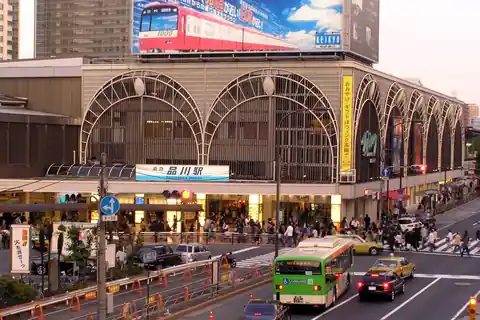 Shinagawa Station exterior in Tokyo, with an arched facade, a green bus, and taxis on the street