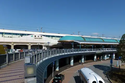 Maihama Station in Urayasu with a teal canopy, a curved elevated walkway, and a white bus in the foreground