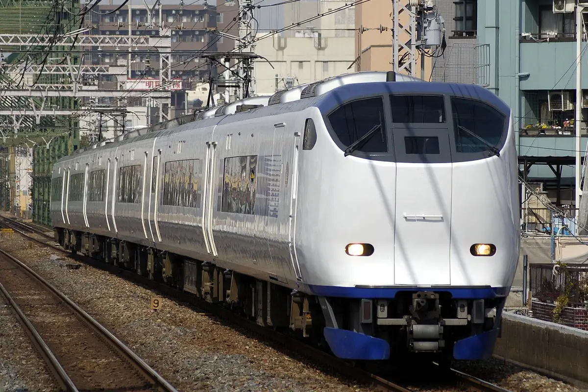 行驶在地面轨道上,后方可见公寓与电线的JR西日本281系HARUKA 特急列车