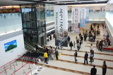 Interior of Ibaraki Airport terminal with welcome banners and passengers walking past an escalator