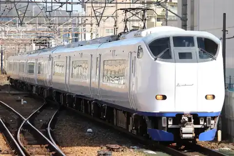 A JR West Haruka limited express train on the Kyoto Line, with overhead wires and buildings behind it