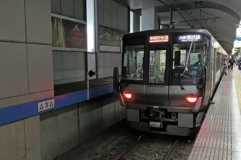 JR West 223 series train showing Kansai Airport Rapid on its front display, stopped at a station platform