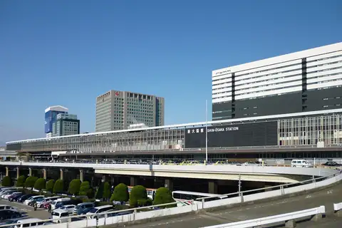 Shin-Osaka Station building with an elevated road and buses in front, and cars parked in a lot below