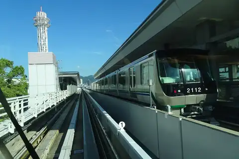 A Port Liner train on an elevated track at Minatojima Station in Kobe, with mountains in the distance
