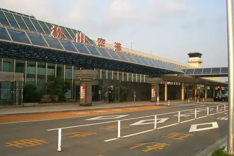 Matsuyama Airport terminal exterior with red Japanese lettering above the entrance and a pickup area on the road