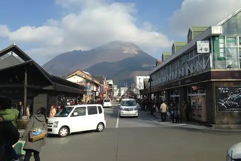 Mount Yufudake rising behind Yufuin Onsen Street, a shop-lined road with cars and pedestrians