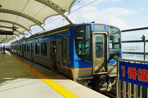A blue and silver Sendai Airport Access Line train at Platform 1, under a curved white canopy