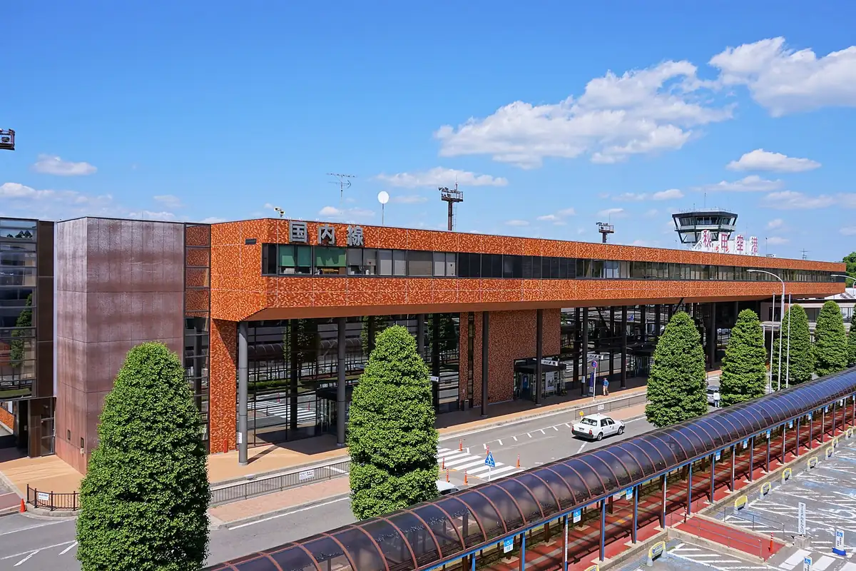 オレンジ色のタイル張り外壁とガラス窓の秋田空港ターミナルビル外観、手前に整えられた木々