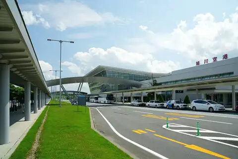 Exterior of Asahikawa Airport terminal building with a curved glass facade and buses and taxis lined up outside