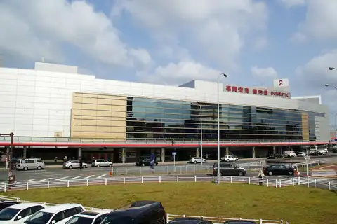 Exterior of Fukuoka Airport's domestic terminal building with its name sign and a parking area in front