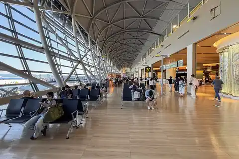 Wide terminal corridor at Kansai Airport with a curved ceiling, a seating area, and passengers walking near gate 20