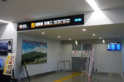 International Arrival Gate signage above glass doors inside Kitakyushu Airport's terminal building