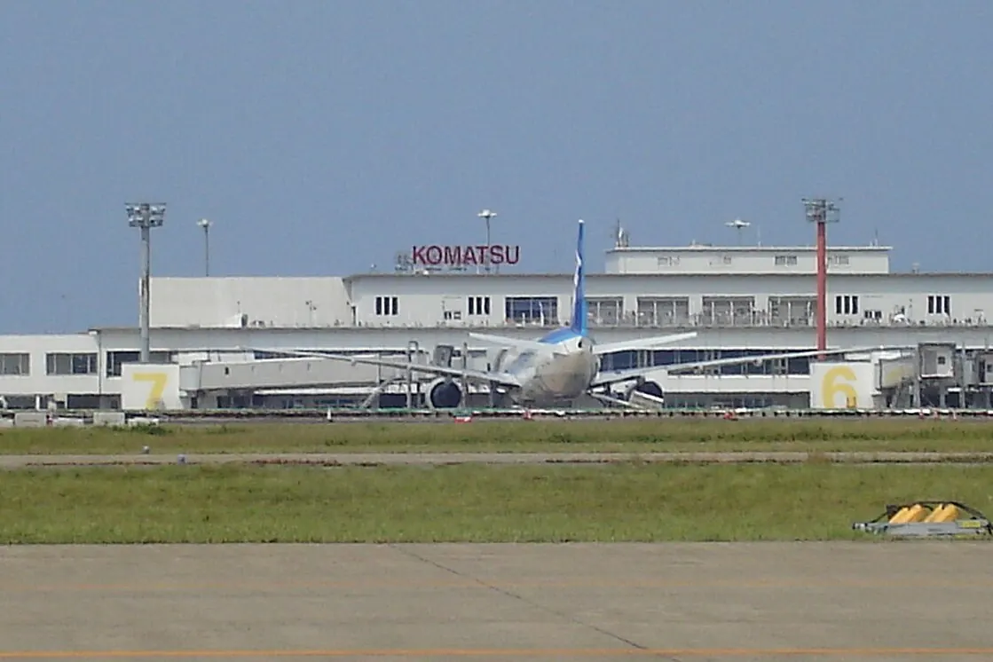 Komatsu Airport terminal building viewed across the runway with an airplane in front and KOMATSU lettering on the facade