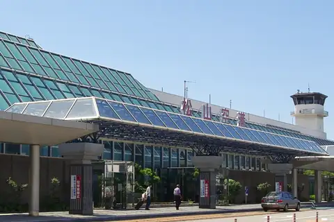 Exterior of Matsuyama Airport terminal building with a glass facade, control tower, and a sign reading Matsuyama Airport