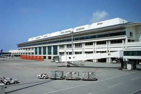 Naha Airport domestic terminal building with a boarding bridge and ground crew pulling cargo carts on the apron