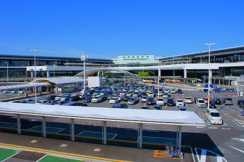 Narita International Airport Terminal 1 building with a curved covered walkway and a crowded parking area in front