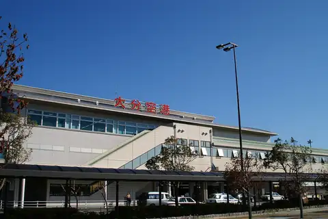 Exterior of Oita Airport terminal building with red signage, trees in front and a small parking area