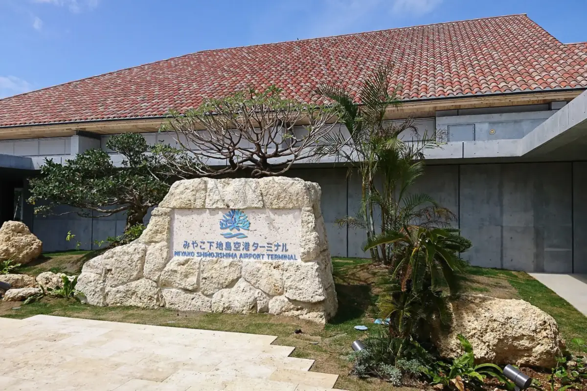 붉은 기와 지붕과 돌 표지판, 야자수가 있는 시모지시마 공항 터미널 건물 외관