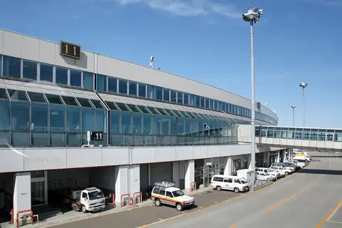 Exterior of New Chitose Airport terminal building with boarding gates and vehicles parked outside