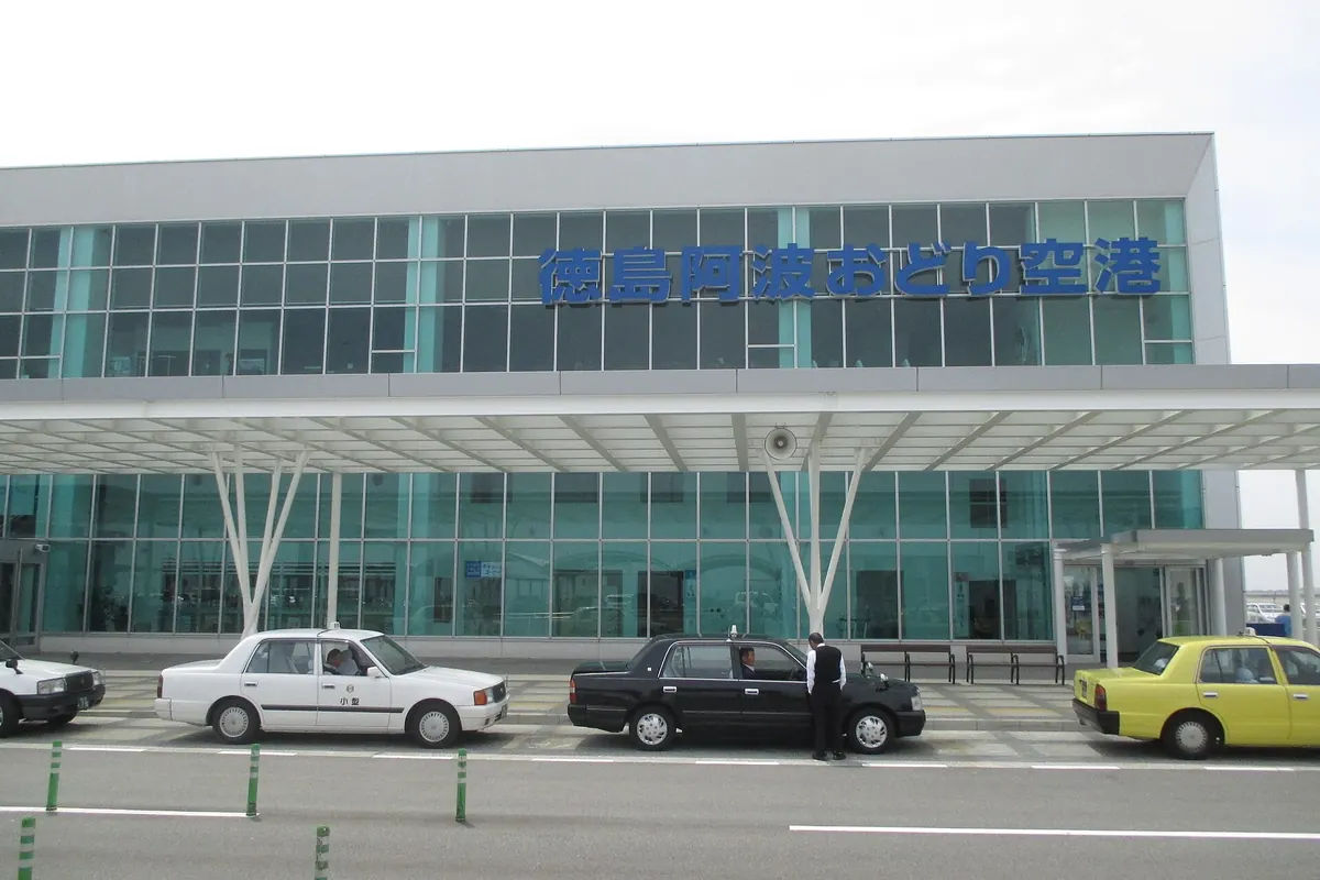 공항 이름 표지판과 밖에 정차한 택시가 있는 도쿠시마 공항 터미널 건물