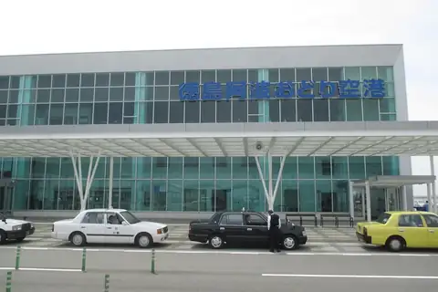 Terminal building of Tokushima Awaodori Airport with its name sign and taxis parked outside
