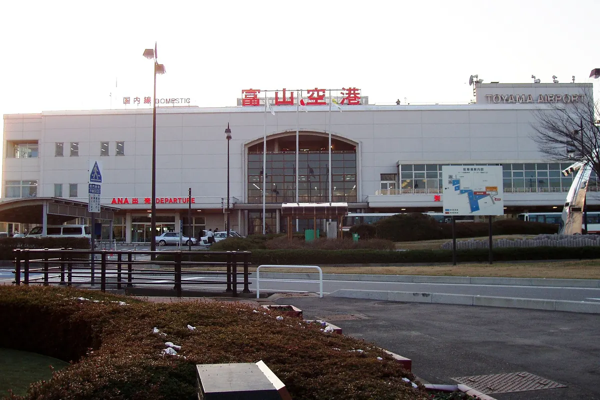 공항 이름 표지판과 밖에 정차한 차량이 있는 도야마 공항 터미널 건물 외관