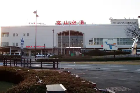 Exterior of Toyama Airport terminal building with its name sign and parked vehicles outside