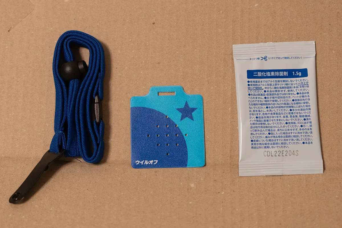 A blue neck lanyard, a light-blue air sanitizer card and a chlorine dioxide sachet laid on cardboard