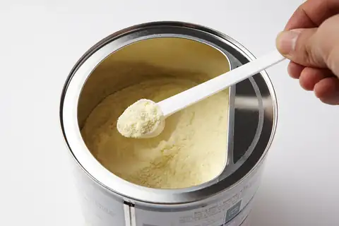 An open can of powdered infant formula with a scoop held by a hand
