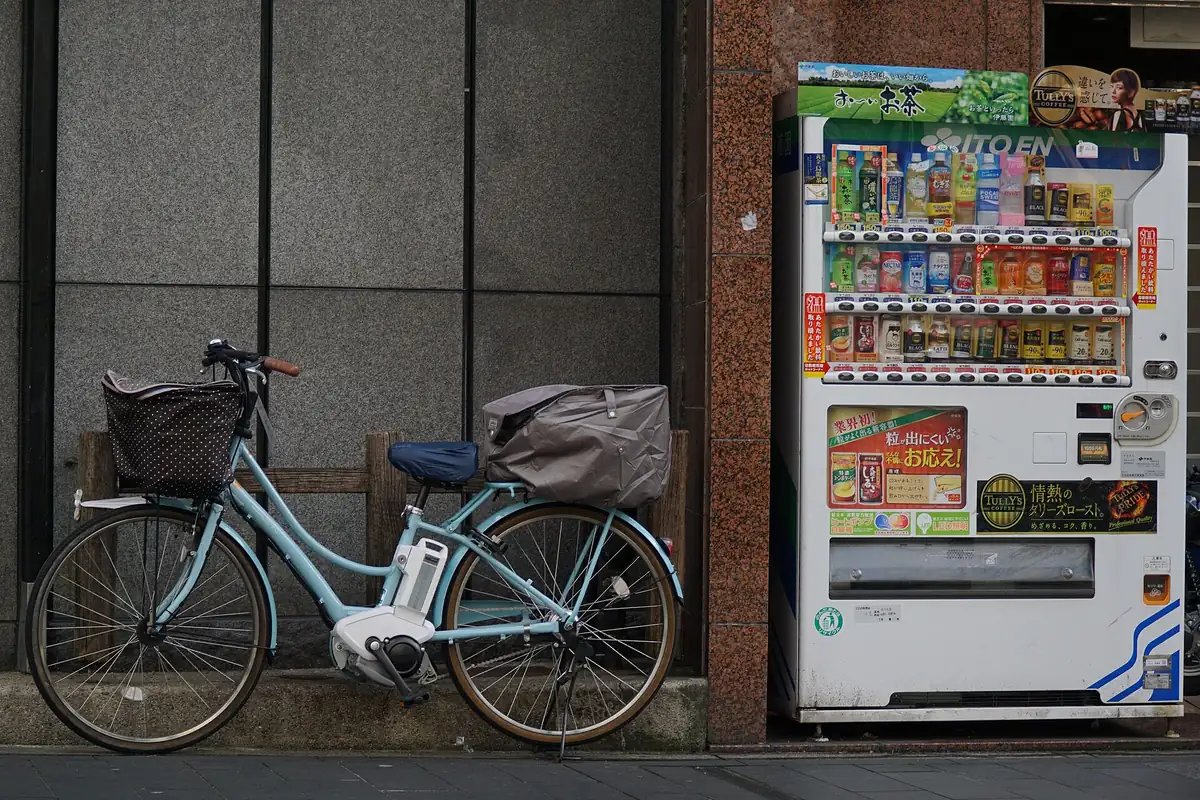 A drinks vending machine stocked with bottled tea and soft drinks on a street in Kyoto, with a bicycle parked beside it