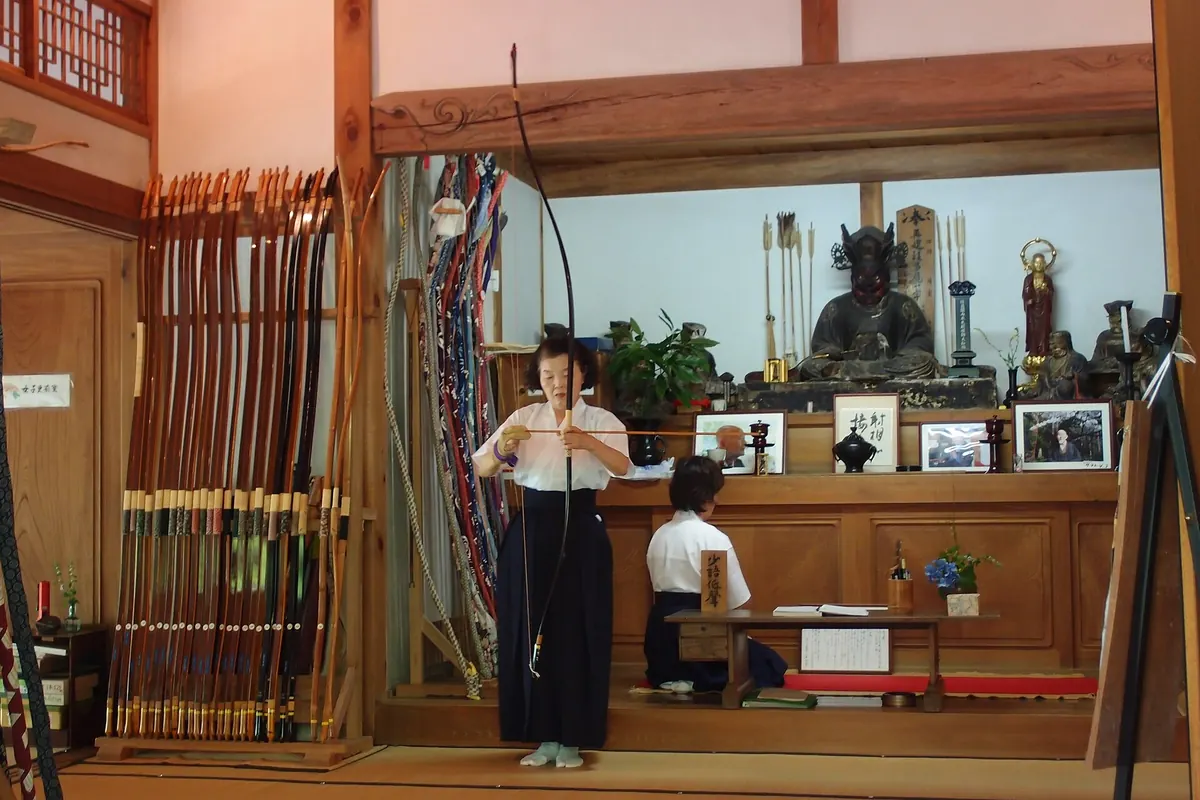 Bows and arrows mounted on the wall of a Kyudo archery hall at Engaku-ji Temple, with a person aiming
