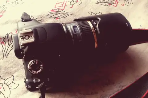 A Canon DSLR camera with a Tamron telephoto zoom lens attached, resting on a patterned cloth