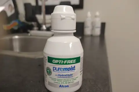 A bottle of OPTI-FREE PureMoist contact lens cleaning solution on a counter