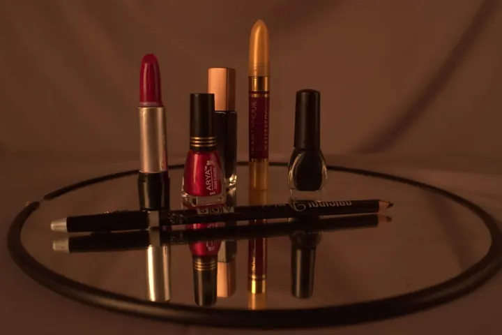A red lipstick, two nail polish bottles, a yellow cosmetic stick, and an eyeliner pencil on a round mirror