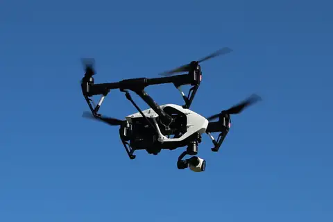 A quadcopter drone with a camera gimbal in flight, seen from below