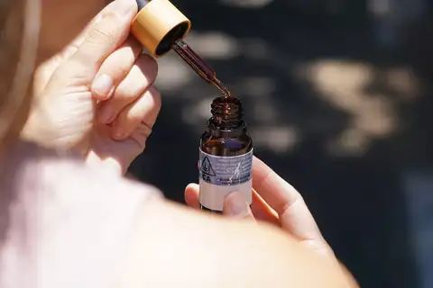 A hand holding a dropper above an open labeled bottle of CBD oil