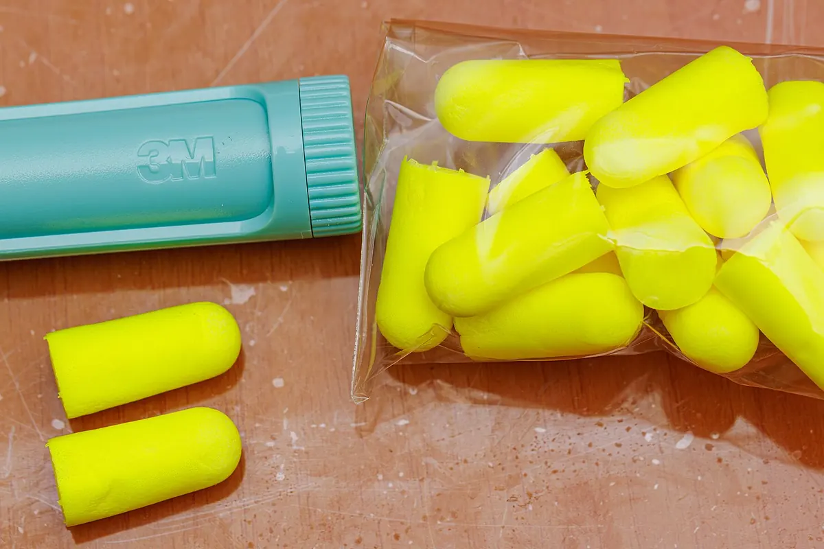 Yellow foam earplugs spilling out of a plastic bag next to a teal 3M carrying case